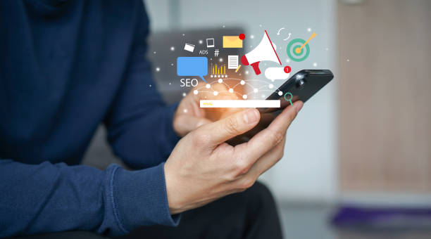 Person holding smartphone with floating SEO, ads, and marketing icons above the screen.