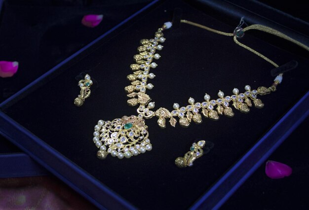 Gold necklace with intricate pendant and pearl accents displayed in a jewelry box, accompanied by matching earrings.